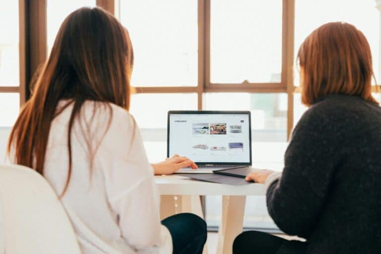 Two women discussing business strategies over a laptop in a bright office.